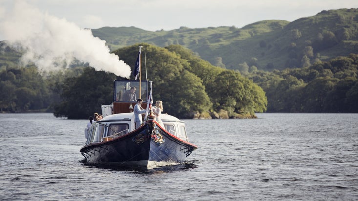 Steam Yacht Gondola steams towards the camera, with a bride and groom in the bow and a tree-covered island behind